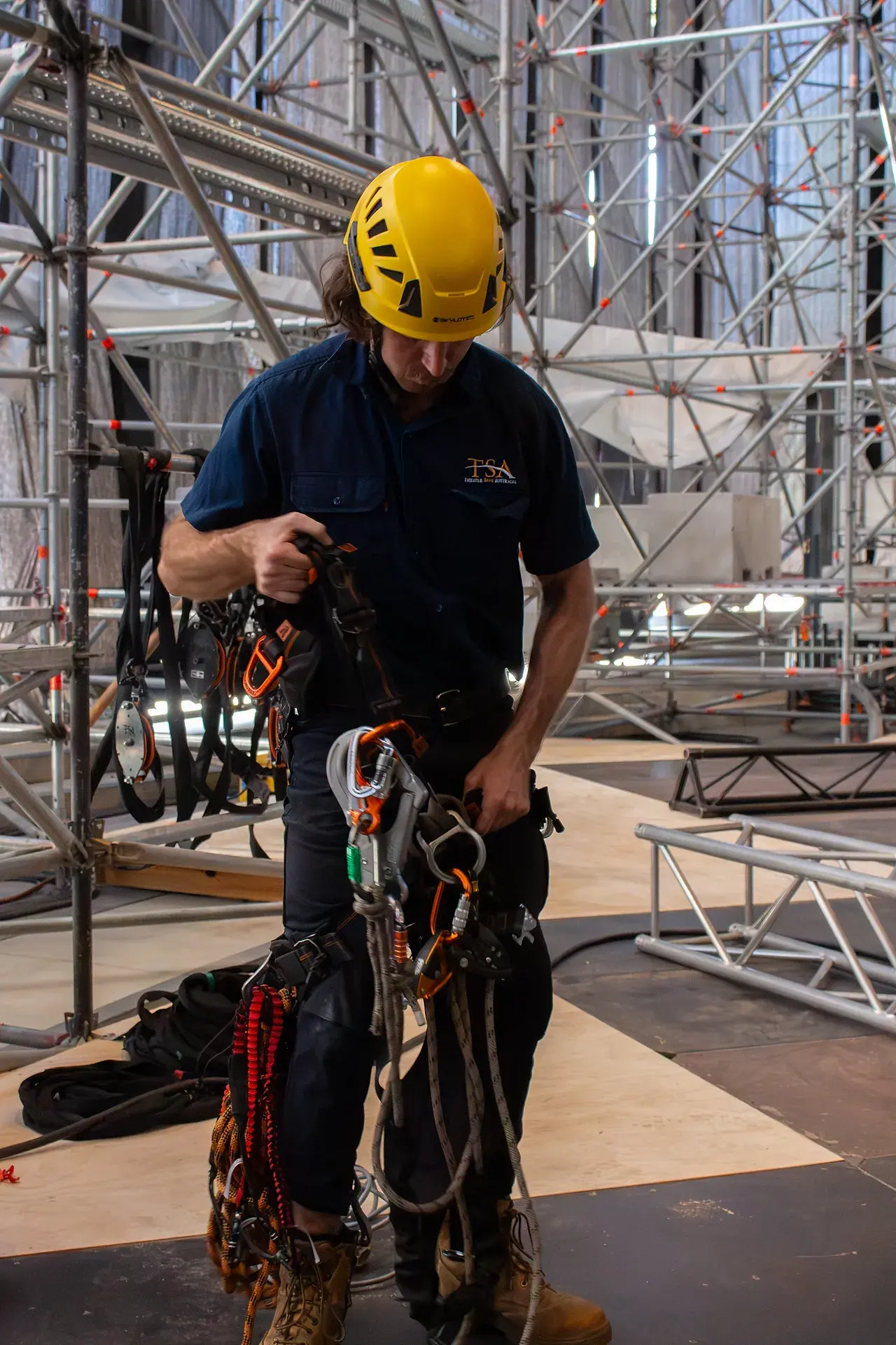 A TSA rigger in helmet and harness sorting rope-access hardware on site
