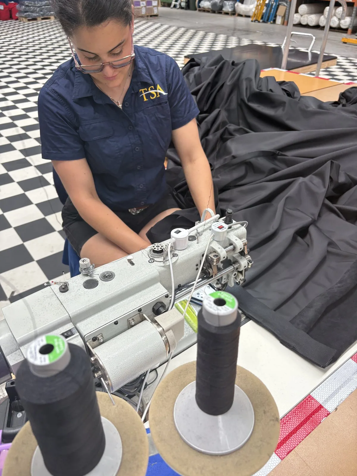 A seamstress at an industrial sewing machine hemming black drape fabric