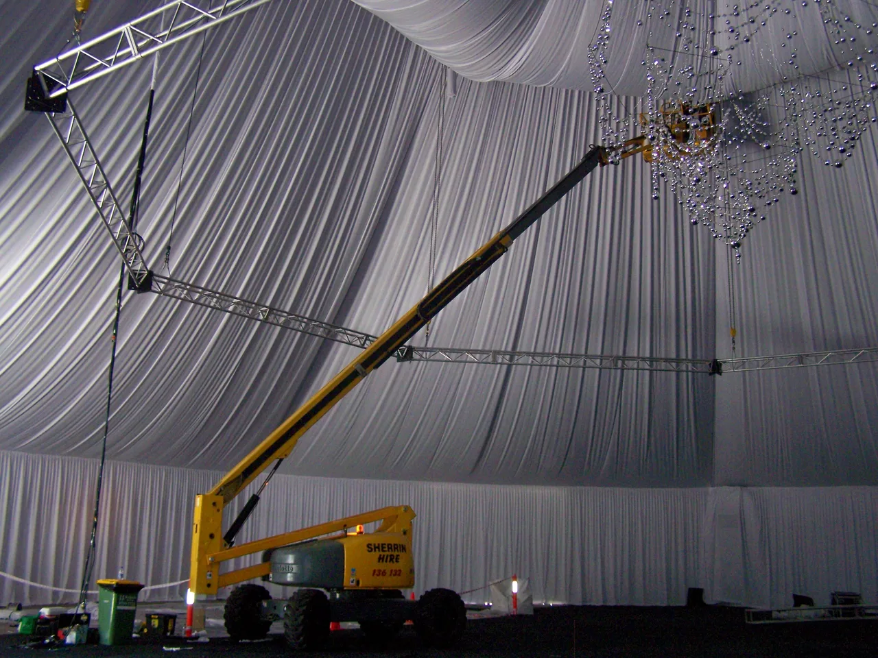 White pleated drape lining the ceiling of a luxury event tent while a chandelier is rigged from truss