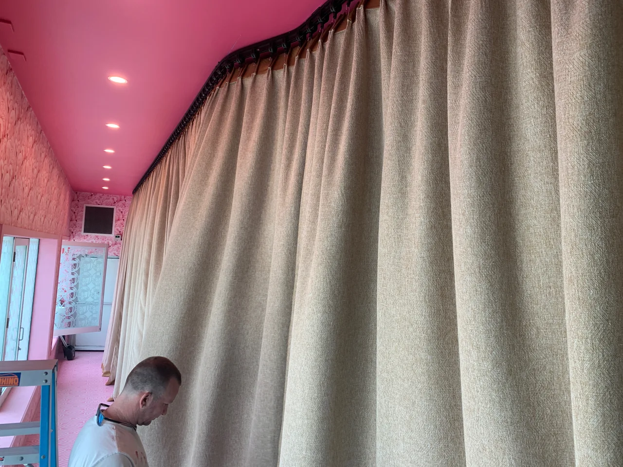 An installer fitting pleated custom drapes to a ceiling track in an interior fit-out
