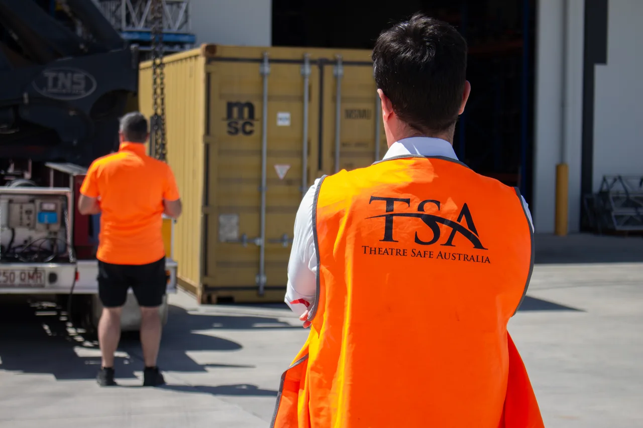 A crane unloading a shipping container at the warehouse while crew watch on