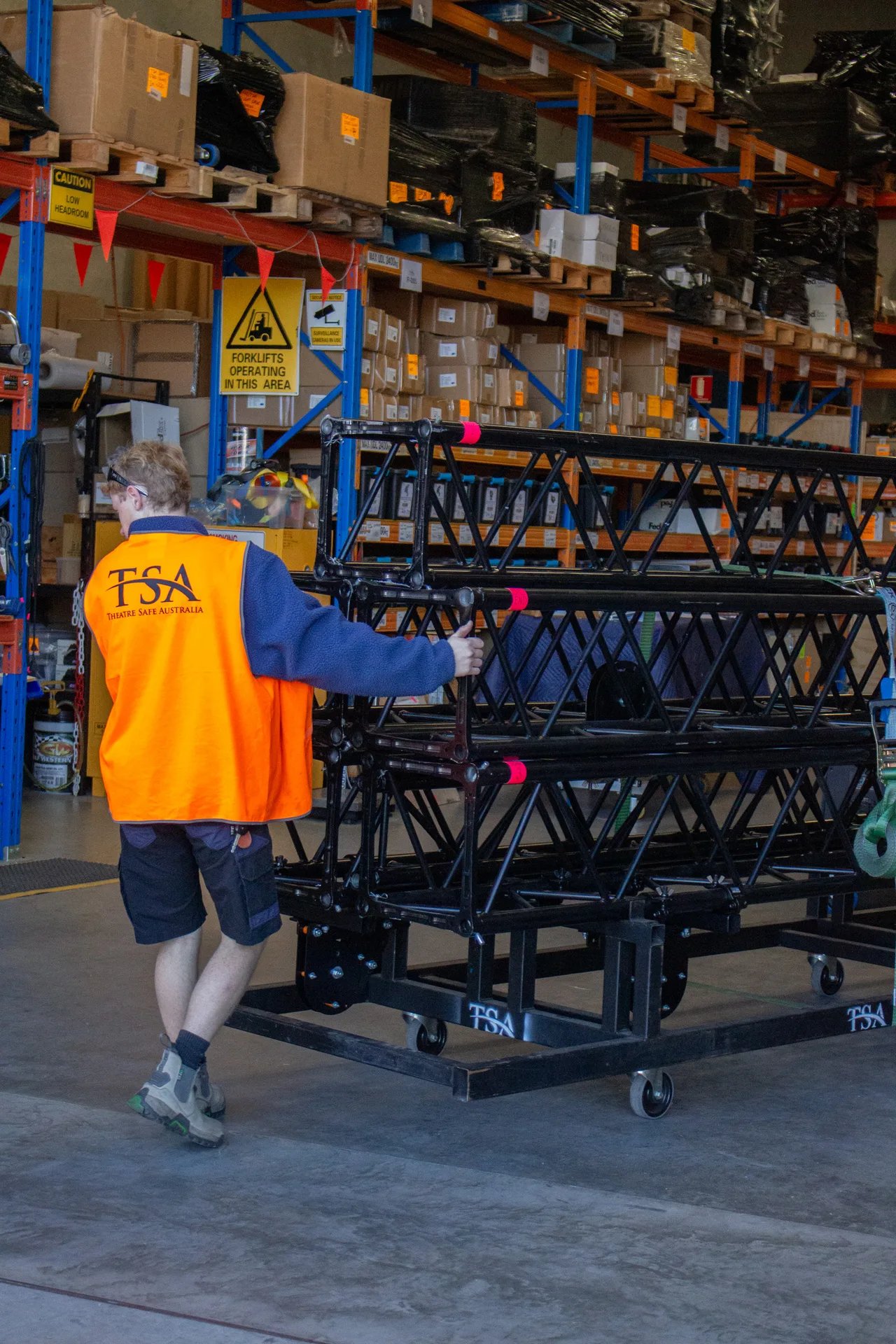 A warehouse worker pushing a wheeled cart stacked with box truss