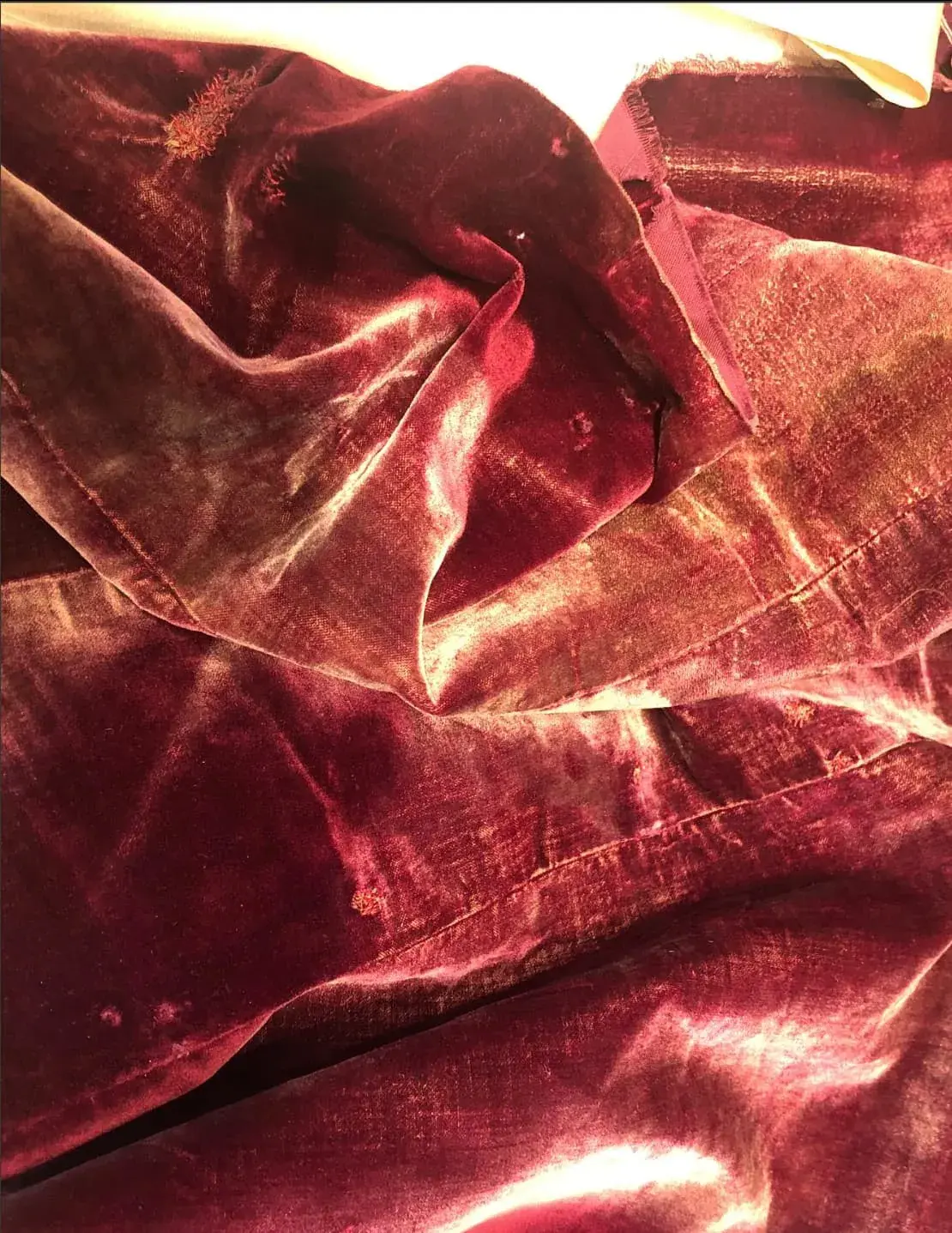 Faded velvet stage drape showing dye loss on the stage-facing surface compared with the deeper colour behind.