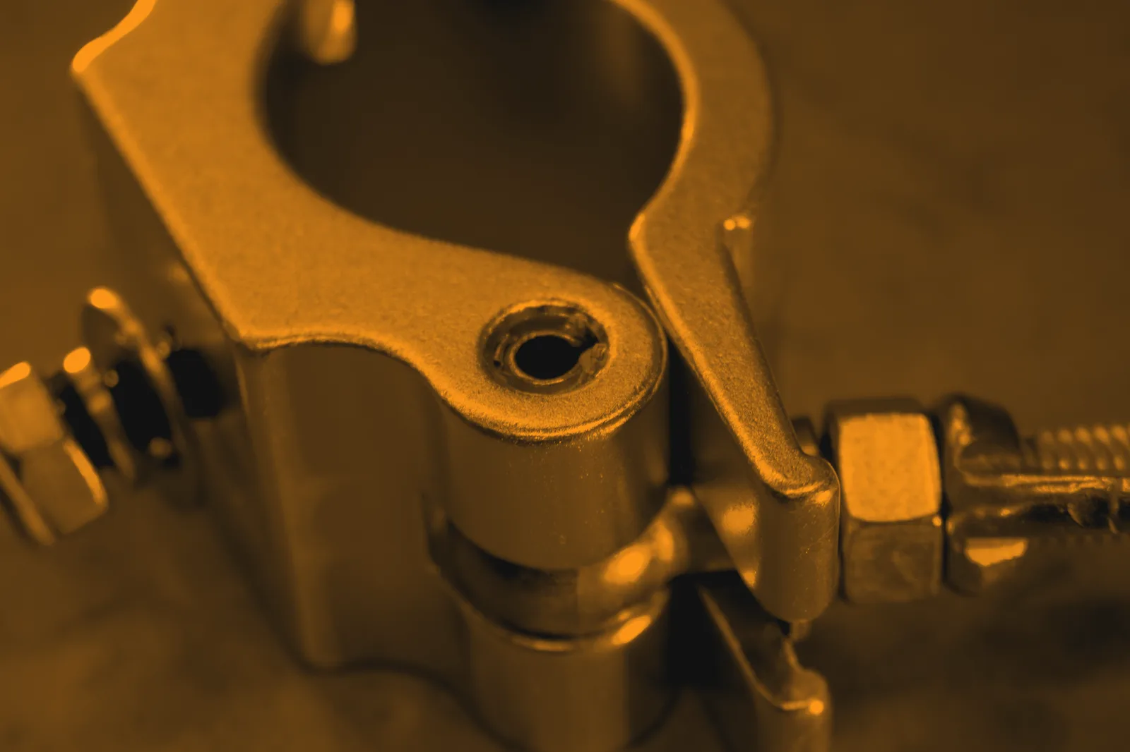 Half coupler jaw closed around a tube, load bolt and nut threaded through the fixed side