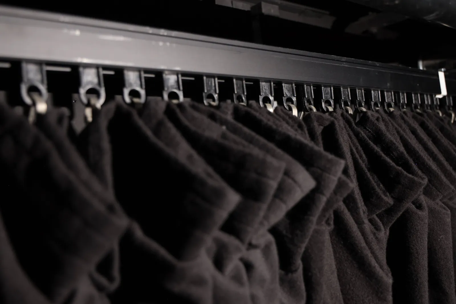 Close-up of track carriers supporting the pleated tops of black wool drapes.
