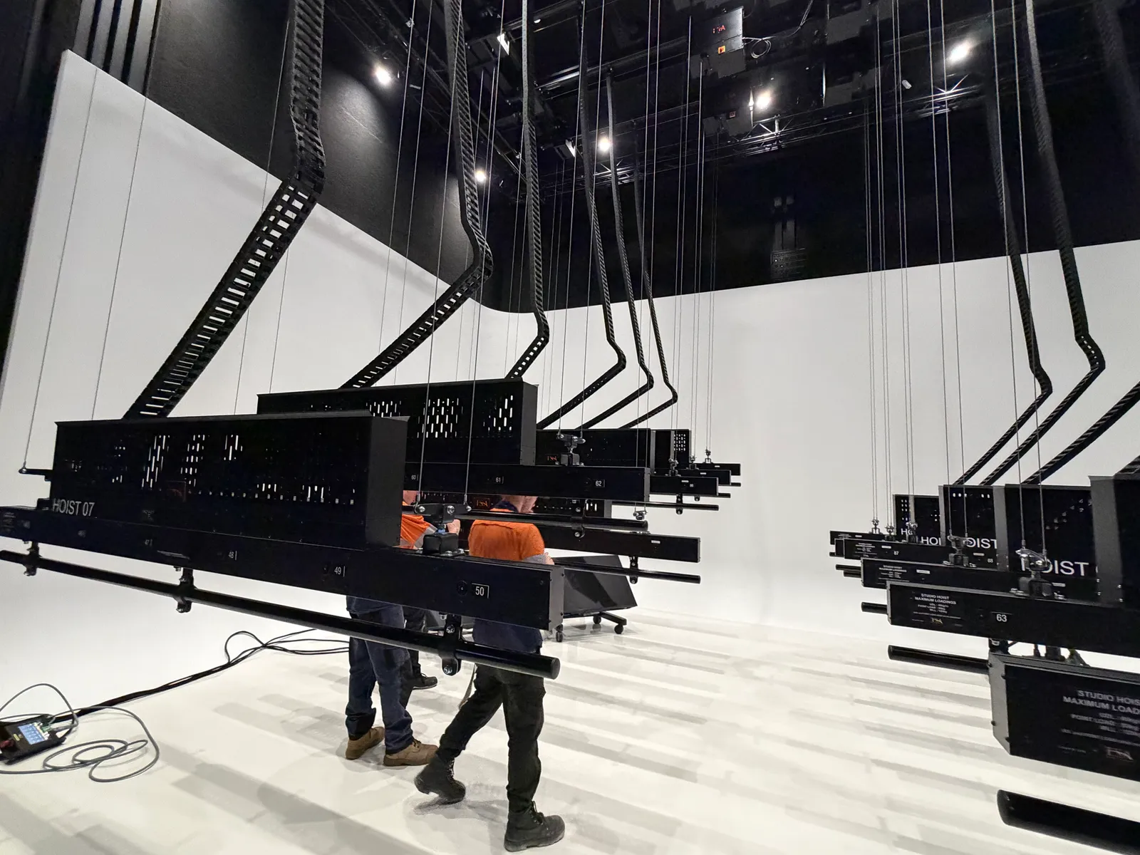 TSA crew setting numbered hoist battens to working height under an installed studio grid, cyclorama wall behind