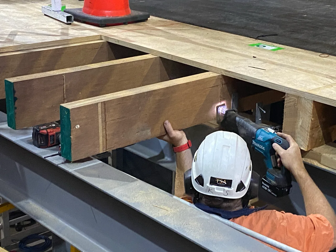Crew cutting timber framing beneath the stage deck