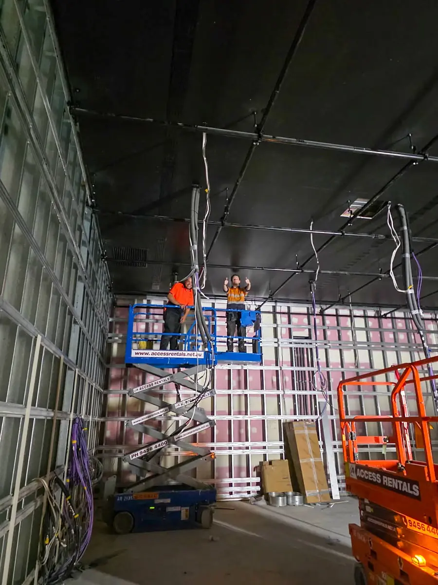 Two crew on an elevated platform installing overhead services, giving a thumbs up.