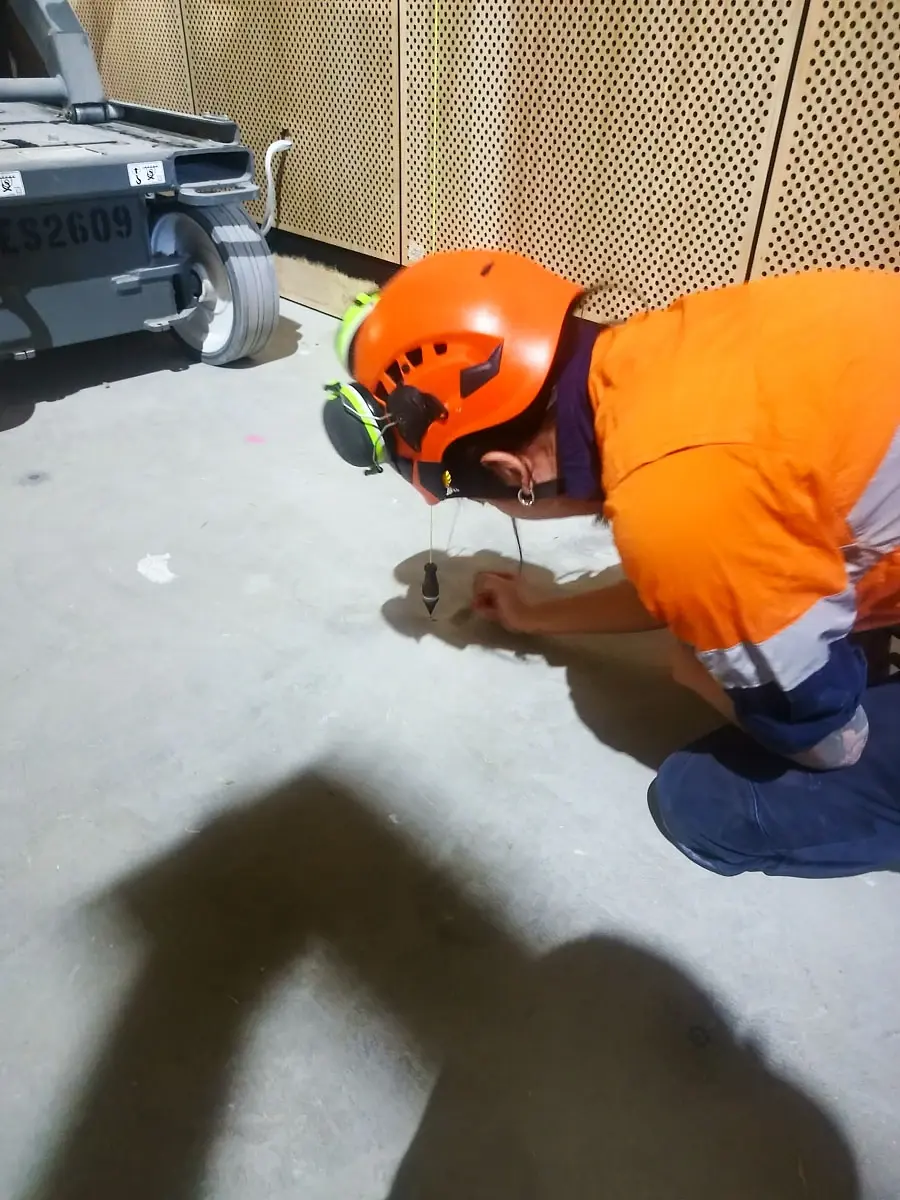 A crew member in a helmet and hi-vis marking out fixing points on the floor.