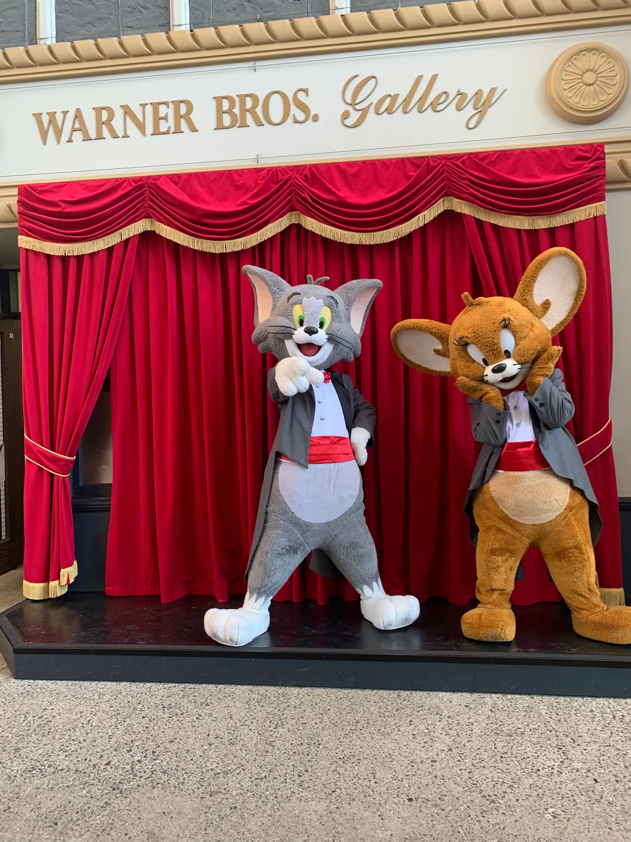 Costume mascots on a small stage in front of red pleated drapes at Movie World
