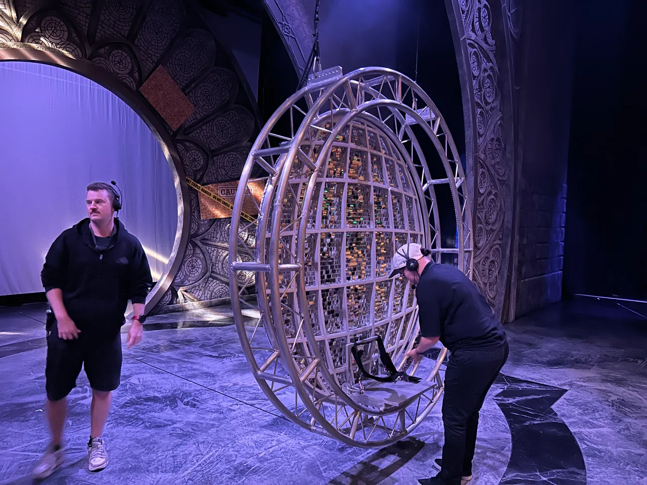 Crew handling a circular truss-framed mirror-ball flying cage during the Sister Act bump-in