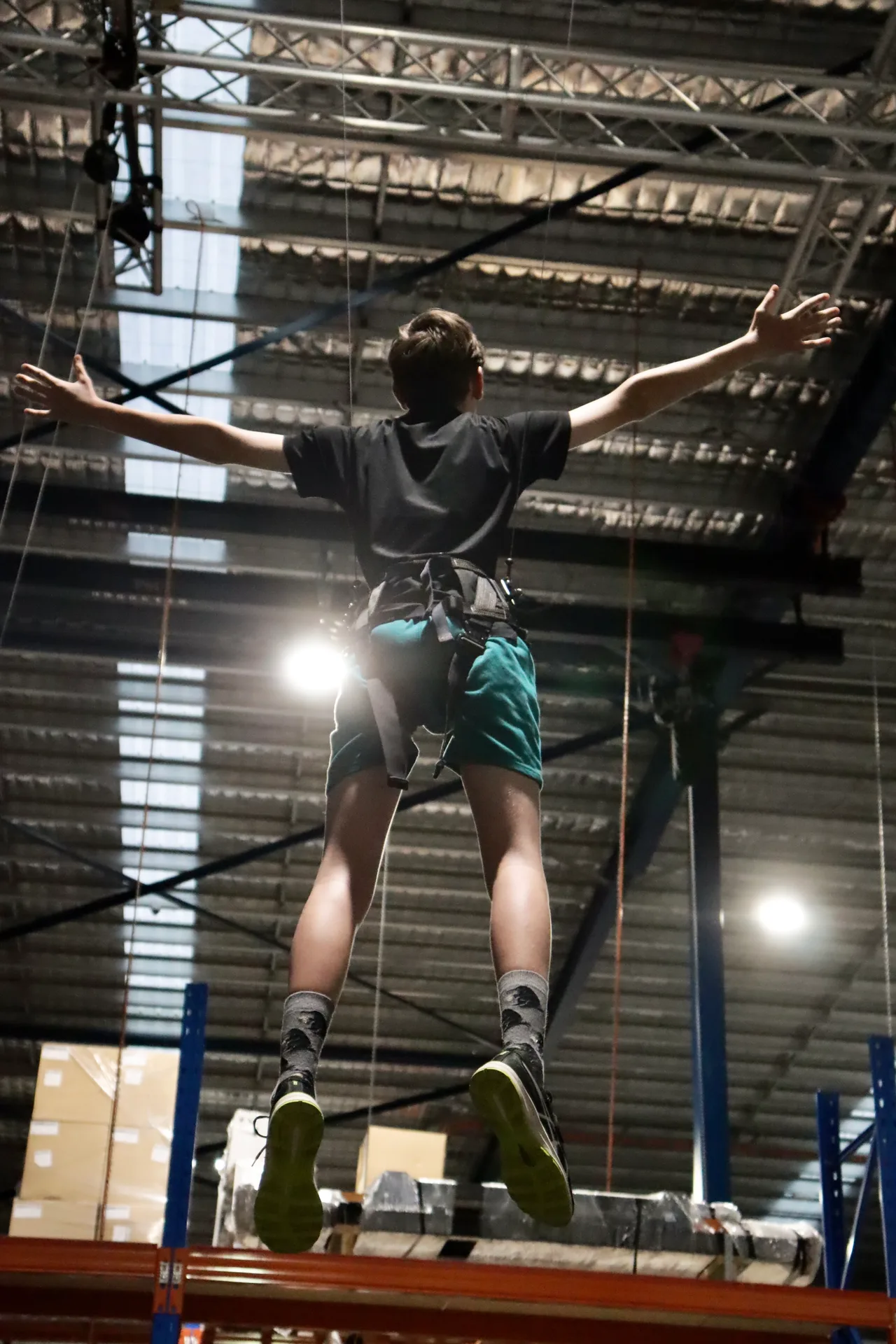 A harnessed performer flown on wires with arms outstretched during a warehouse flying test