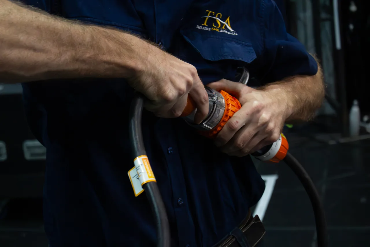 A technician connecting a three-phase power connector backstage at The Star