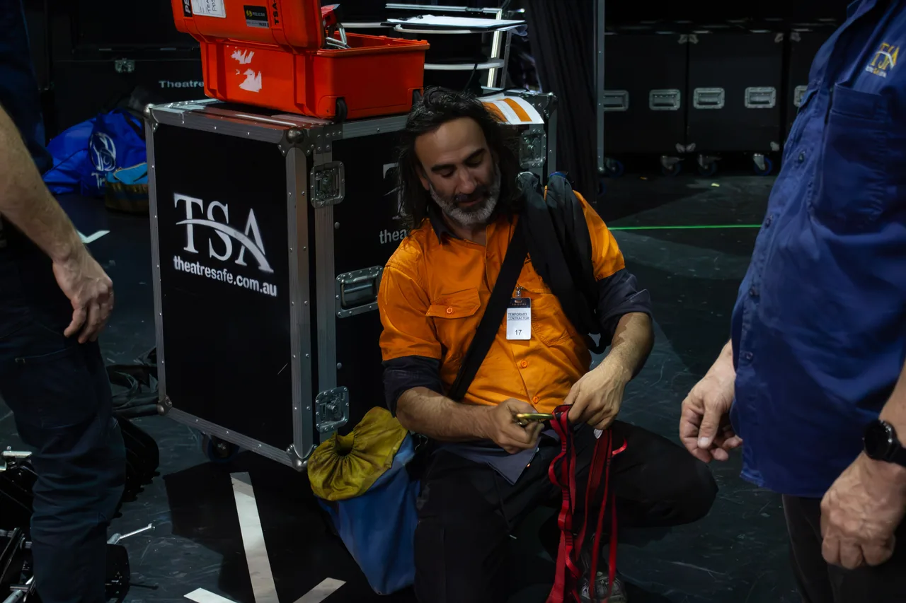 A contractor beside a road case sorting webbing straps during performer flying setup