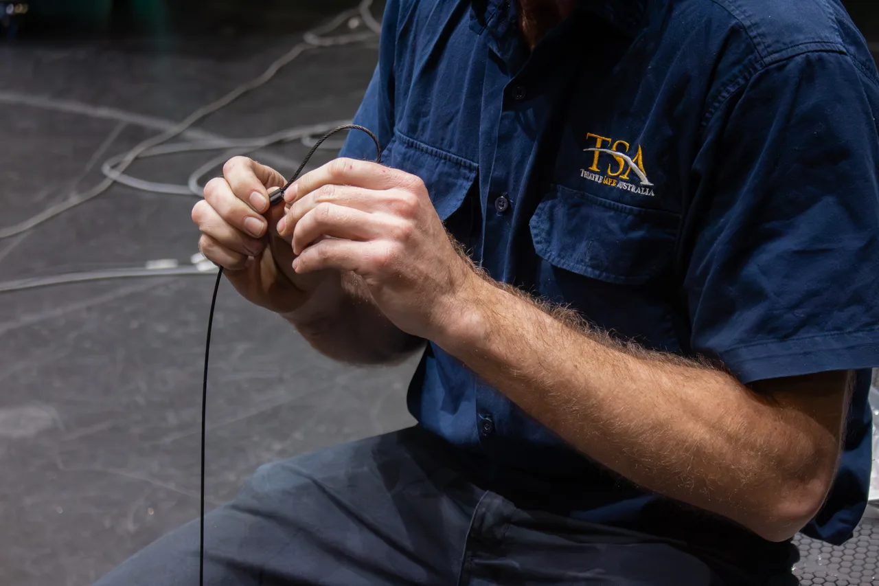 A technician's hands terminating a thin steel wire rope on stage during performer flying work
