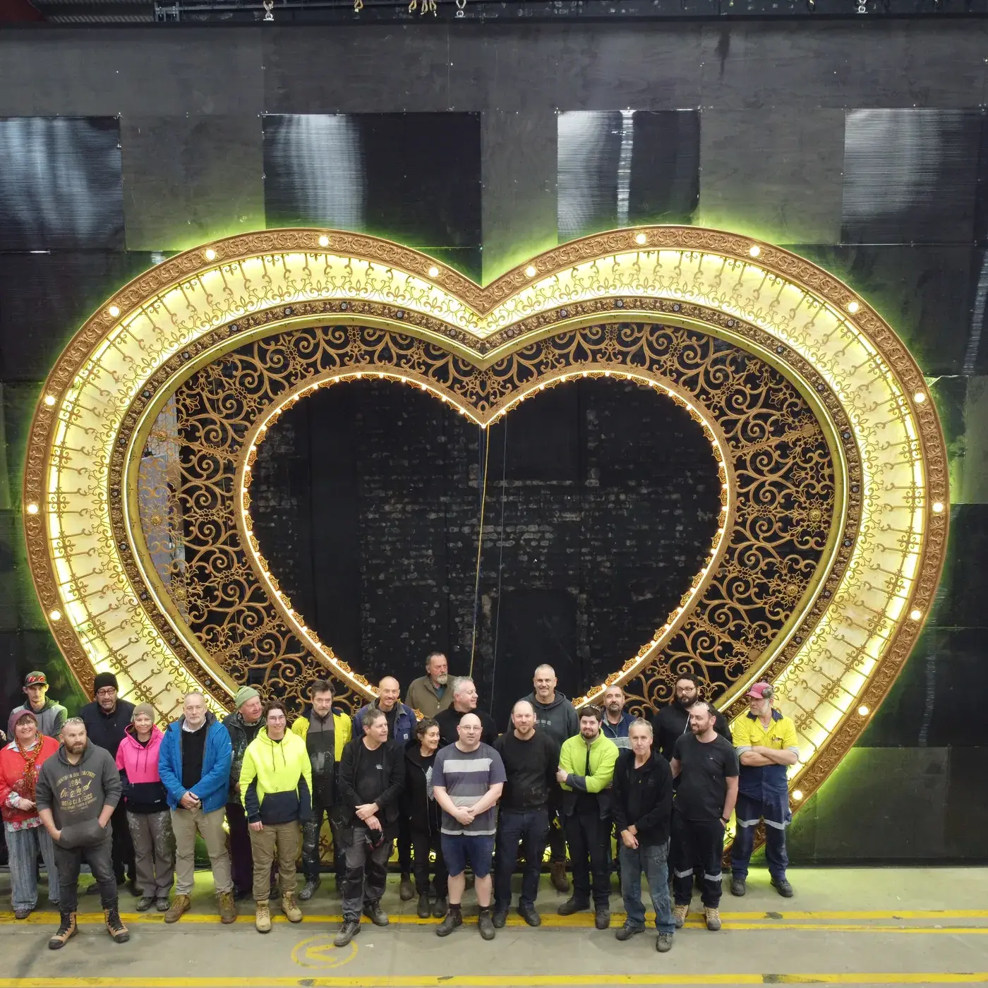The finished, gilded Club Heart Portal lit in the TSA Adelaide workshop, with the crew who built it standing in front