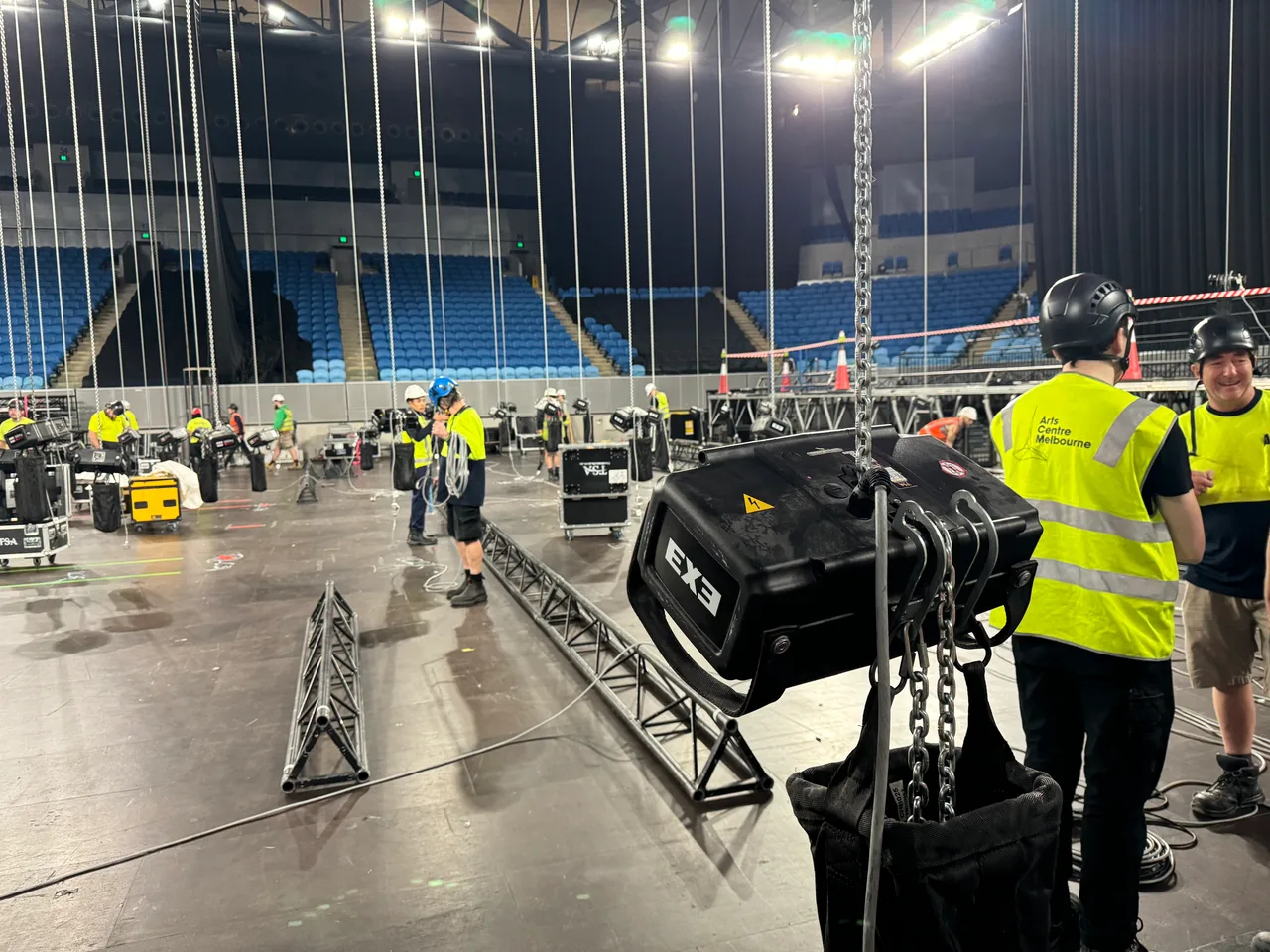 An EXE chain hoist in the foreground of an arena bump-in with truss and crew behind