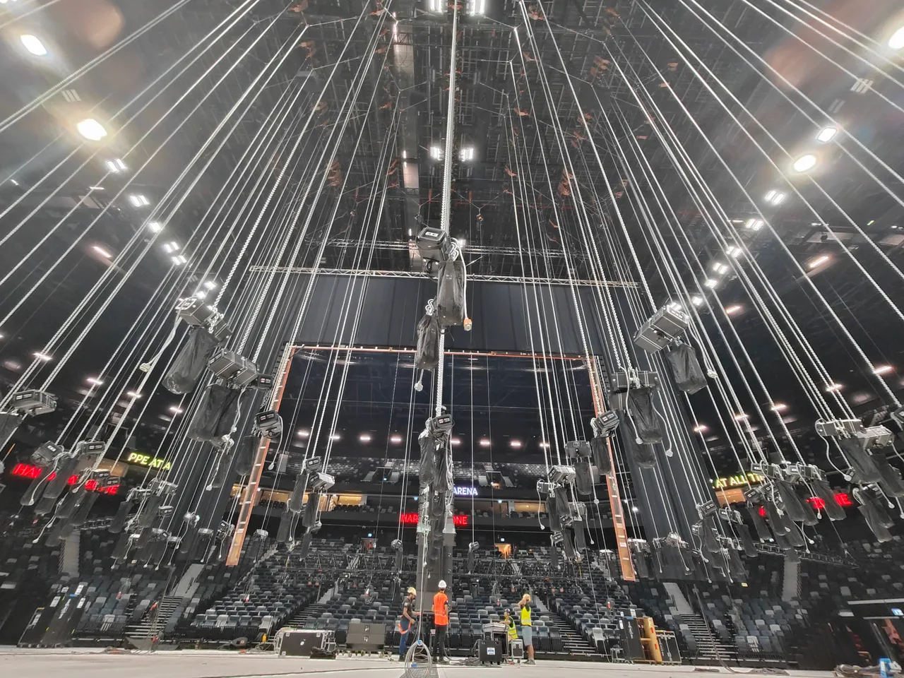 Dozens of chain hoists suspended on rigging lines above the arena floor during a production load-in at Etihad Arena