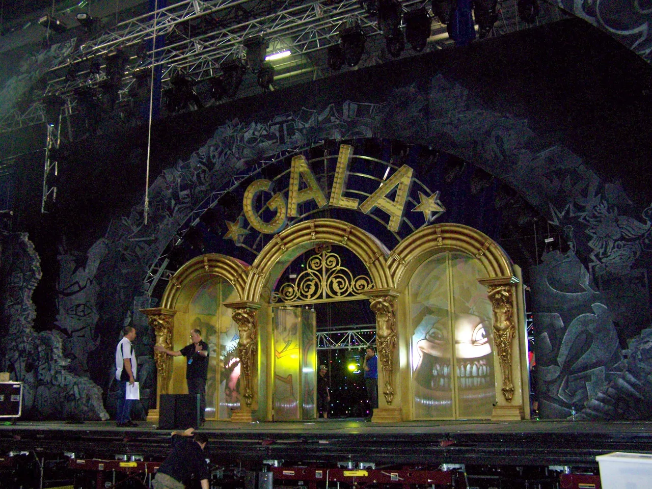 Gold arch set piece with painted surround being prepared on stage for a comedy gala