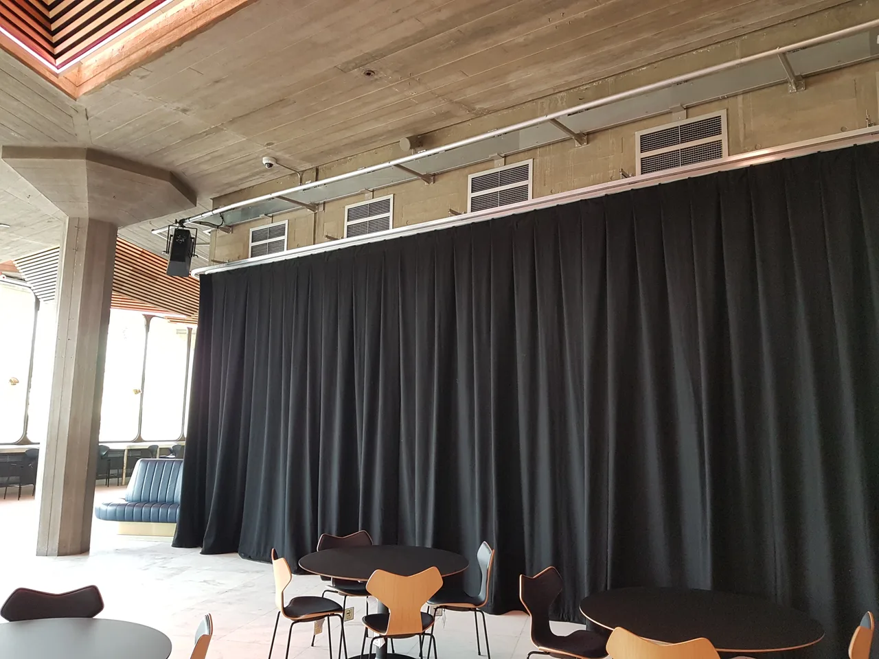 Full-height black drapes on a ceiling-mounted track dividing a concrete-ceilinged foyer